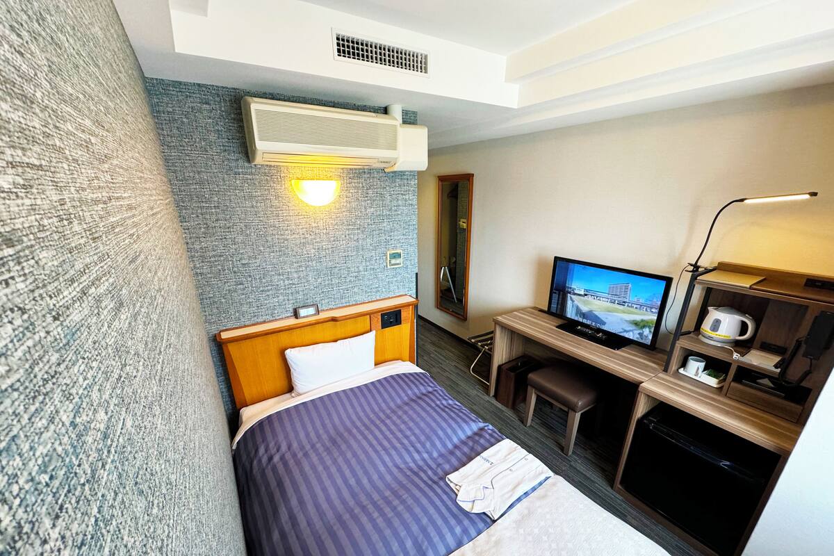 A hotel room with a bed, a desk with a TV, a coffee maker, and a wall-mounted air conditioner.