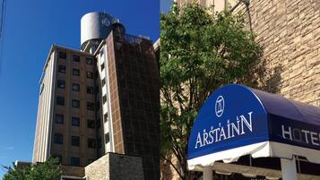 A hotel with a prominent water tank on the building, a stone facade, and a blue awning with the hotel name.