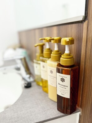 A bathroom with a wooden vanity, a mirror, and a row of shampoo bottles. - Hotel Arstainn (Maizuru)