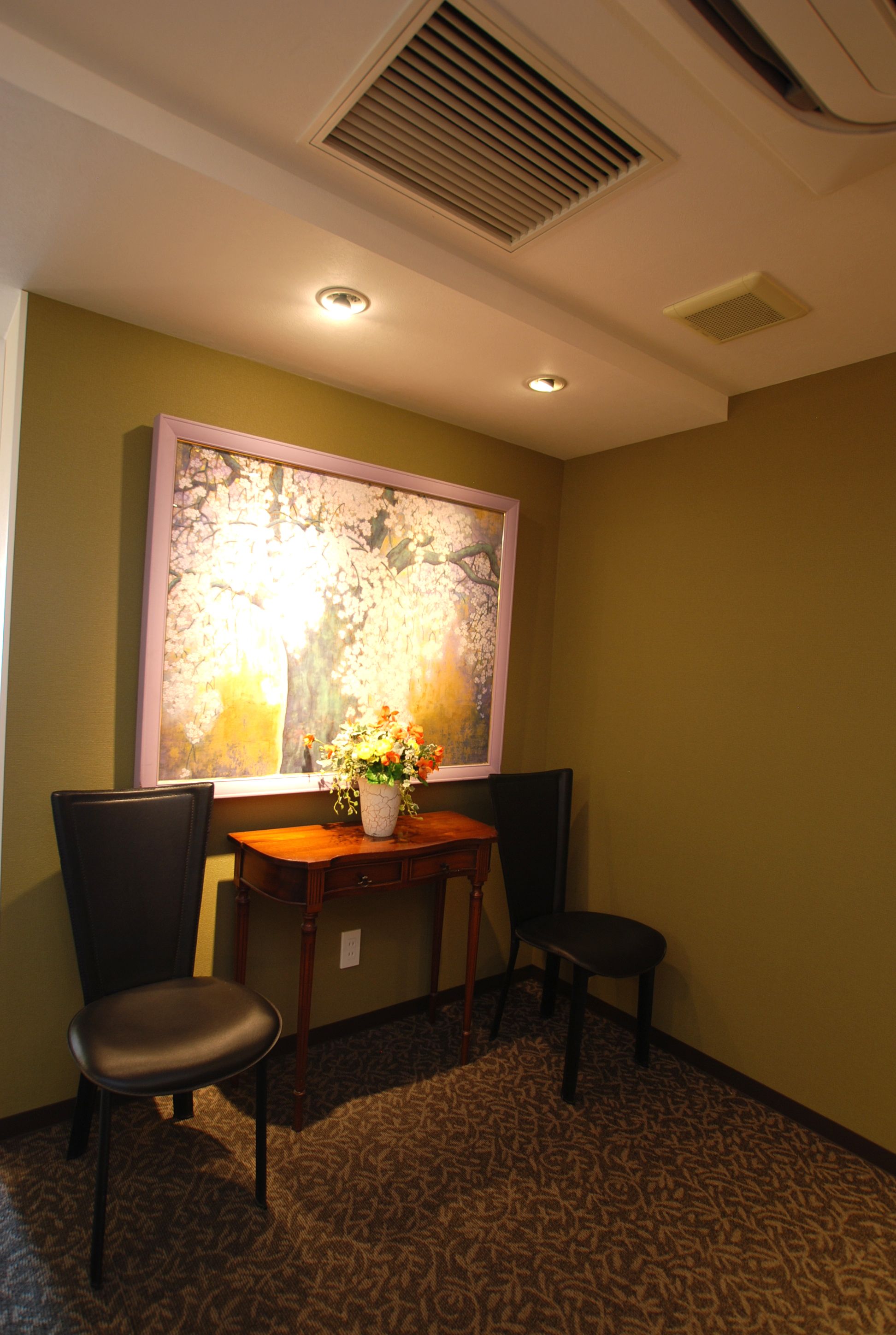 Une pièce comprenant une table, deux chaises, un vase avec des fleurs et un tableau accroché au mur.