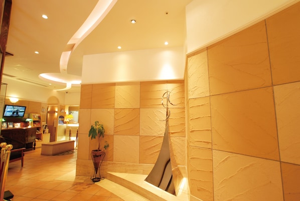 A lobby with a reception desk, a television, a plant, and a modern sculpture. - Hotel Arstainn (Maizuru)