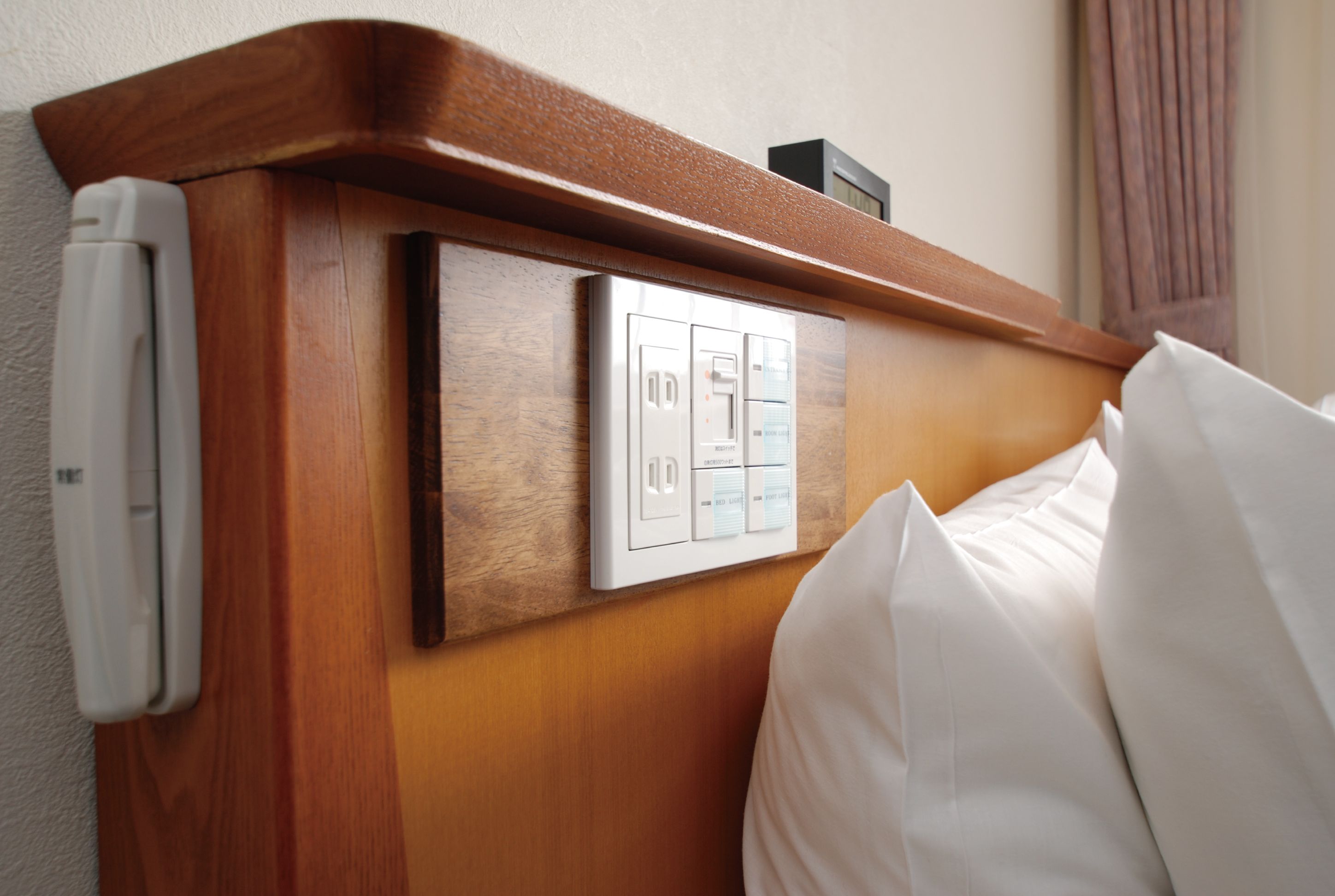 Ein Hotelzimmer mit einem Holzkopfstück, einer Steuerung mit mehreren Tasten und einem weißen Kissen.