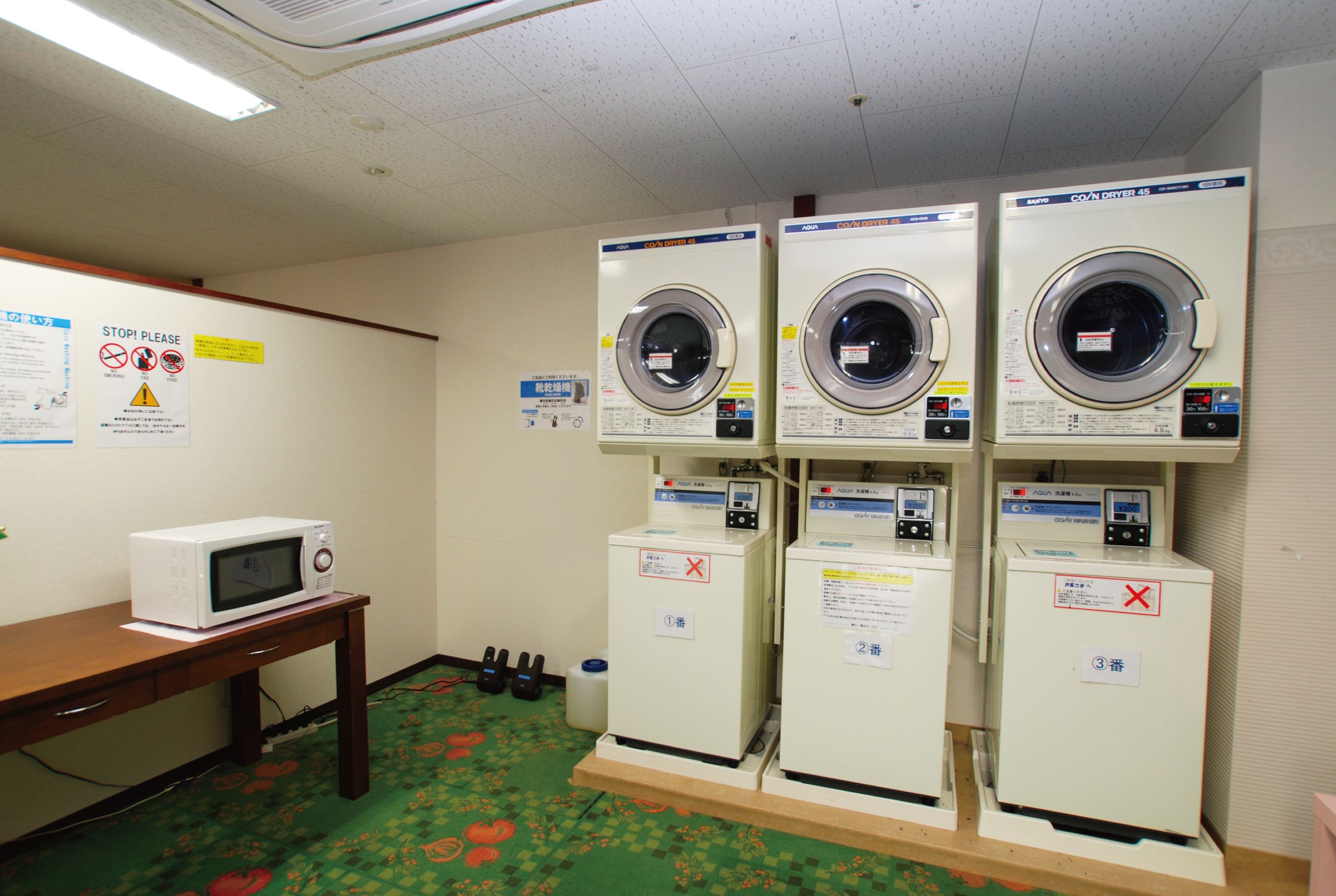 A laundry room with four washing machines, a microwave, and a wooden table.