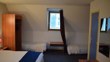 Habitación de hotel con dos camas individuales, un armario de madera, una mesita pequeña, una ventana con cortinas y un televisor en la pared.