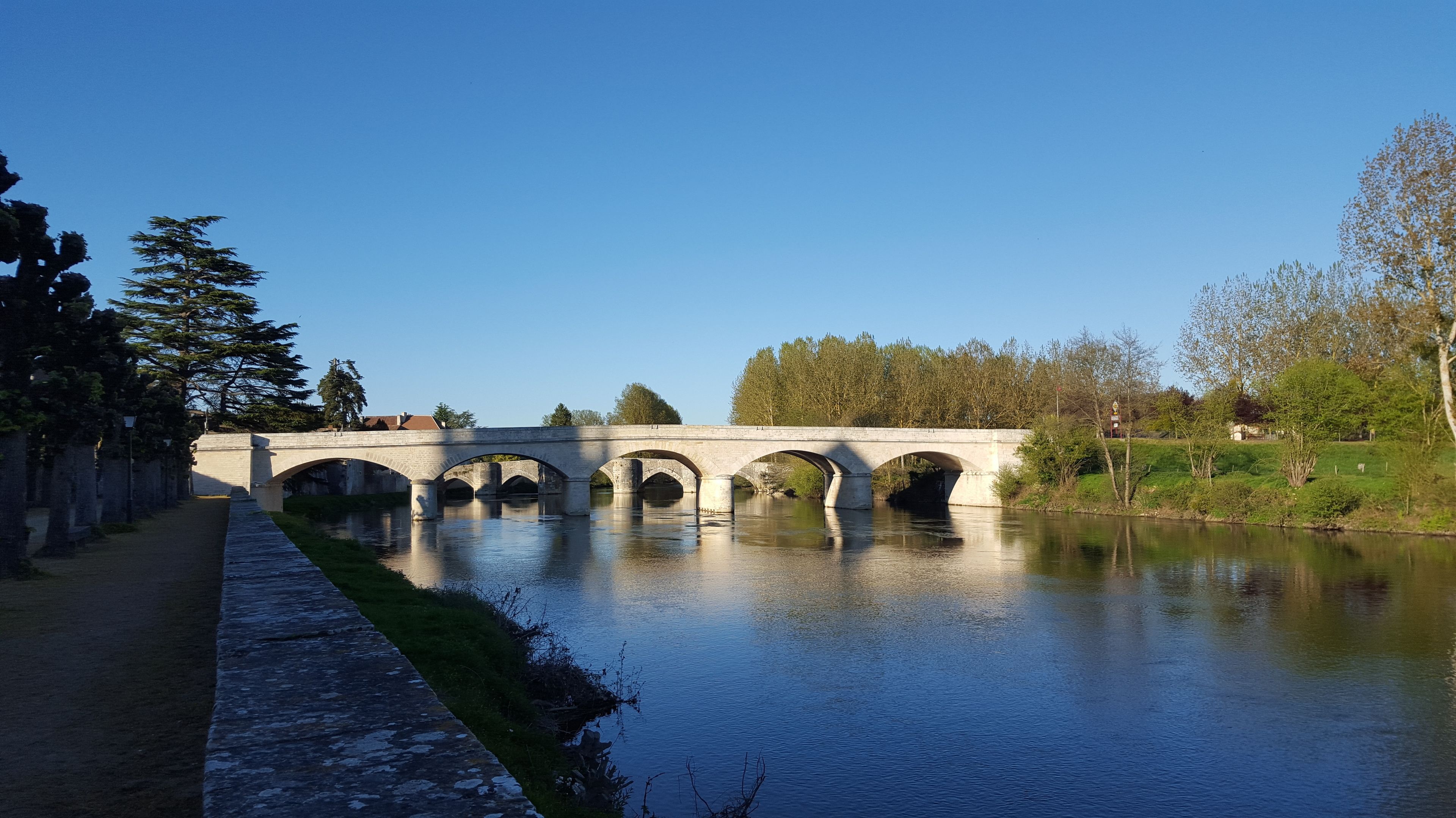 Un puente de piedra sobre un río tranquilo con un camino a la izquierda.