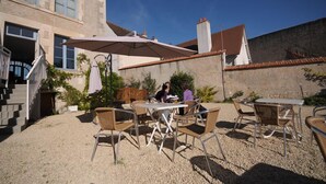 An outdoor patio with tables and chairs, a covered seating area, and a building with a staircase and windows. - Hôtel de France (Saint-Savin)