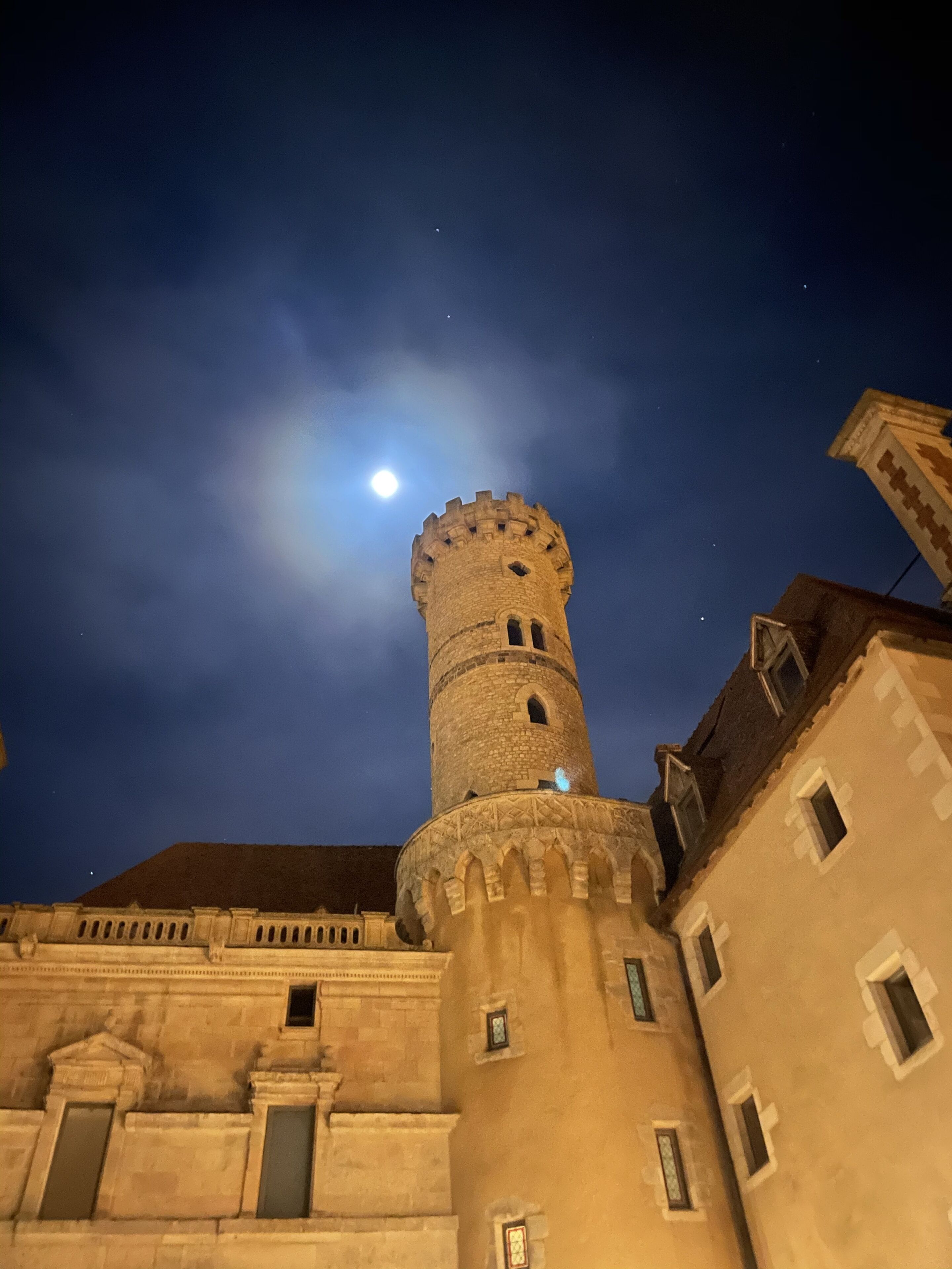 Una torre histórica con un cielo iluminado por la luna, parte de un complejo arquitectónico más amplio con ventanas y detalles arquitectónicos visibles.