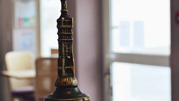 Una campana de bronce sobre una mesa de madera en una habitación con ventanas amplias y una silla al fondo.