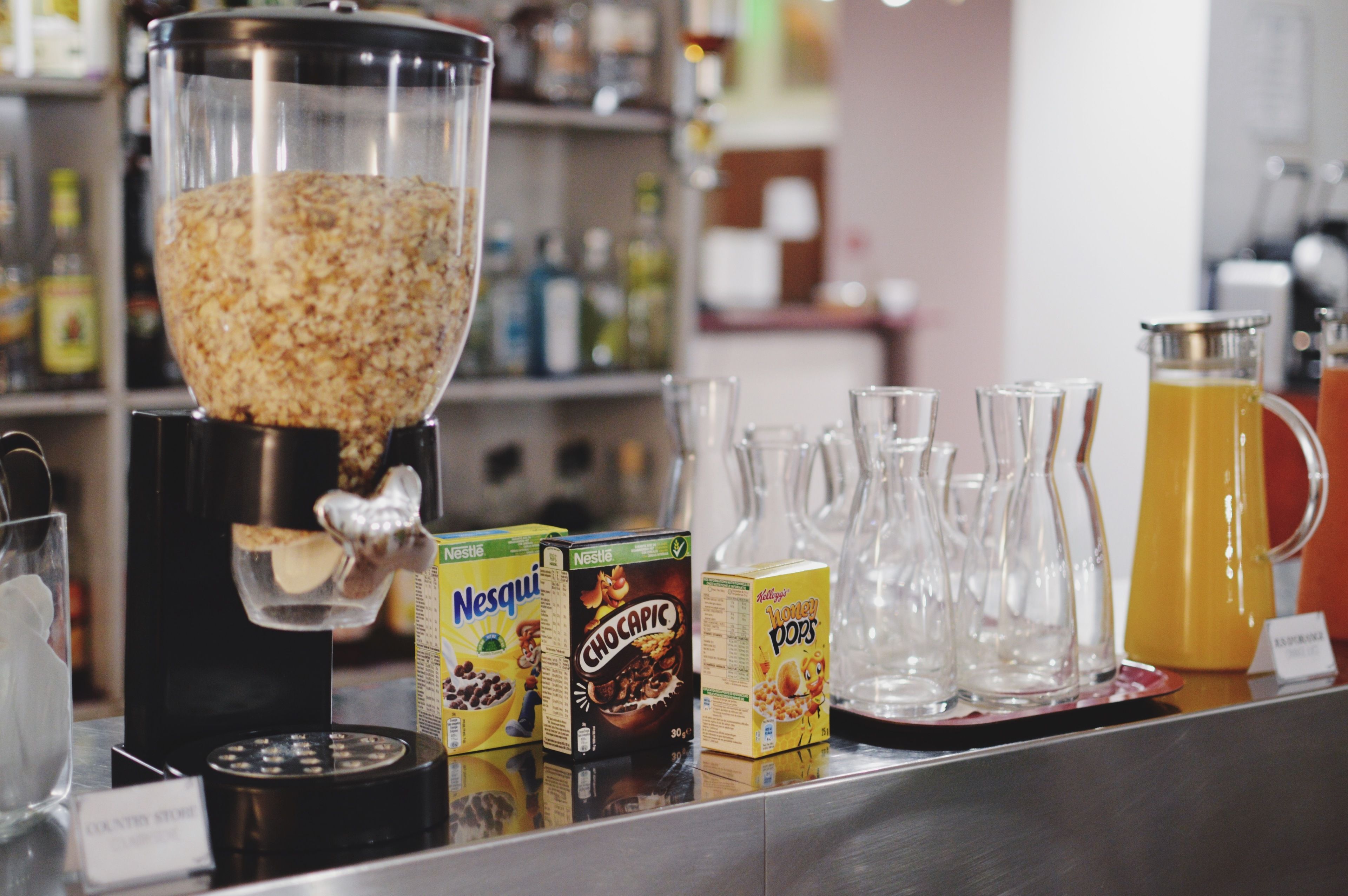 A cereal bar with various boxes of cereal, a coffee machine, and several glass pitchers on a counter.
