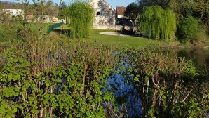 A church with a bell tower, surrounded by lush greenery and a pond. - Hôtel de France (Saint-Savin)
