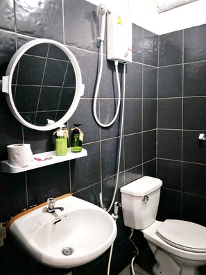 Un baño con un lavamanos blanco, inodoro y cabezal de ducha manual fijado a la pared.