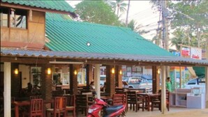 Un restaurante con terraza, una moto roja estacionada adelante y un edificio con techo verde.