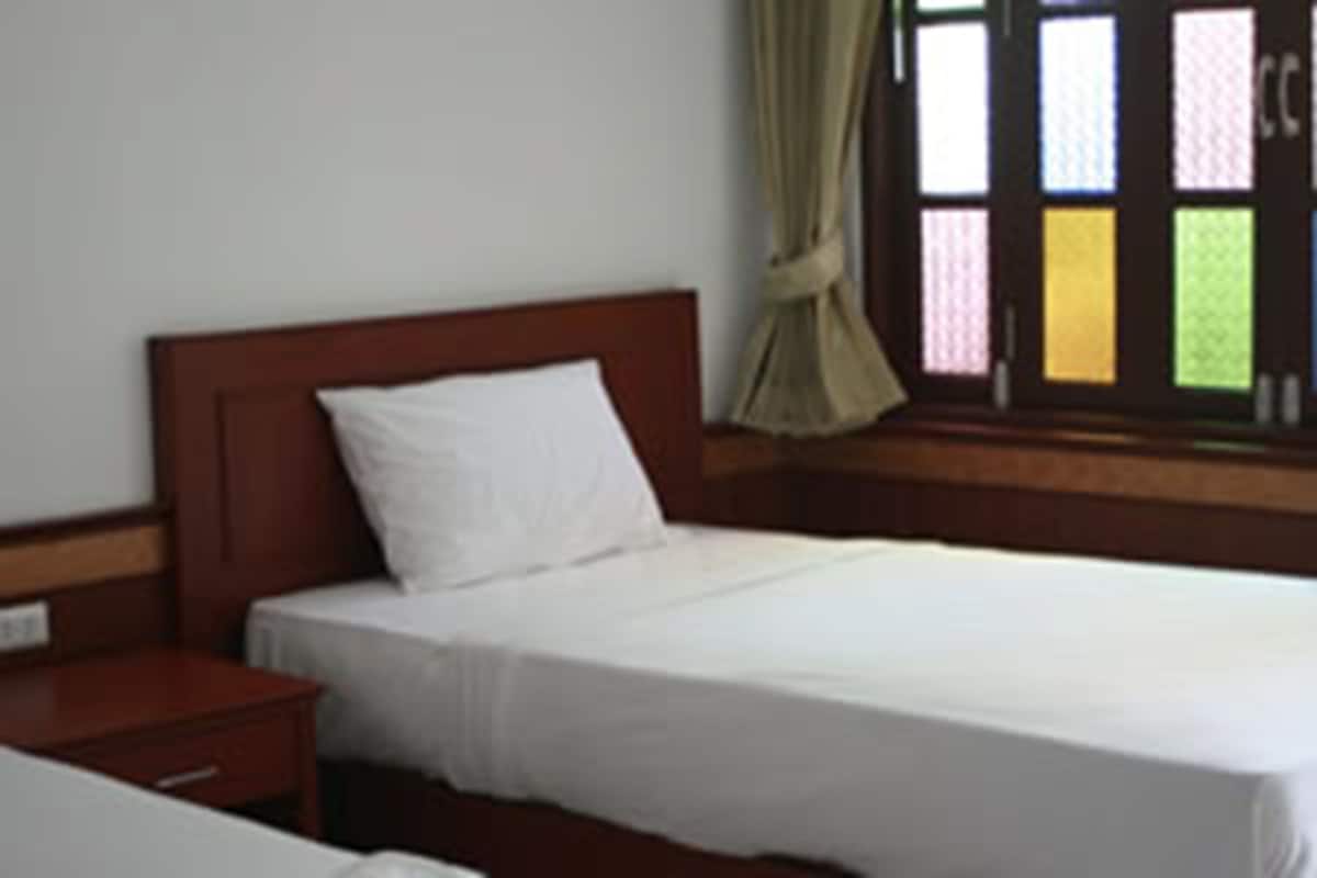 A single bed with a wooden headboard, a bedside table, and a window with a curtain.