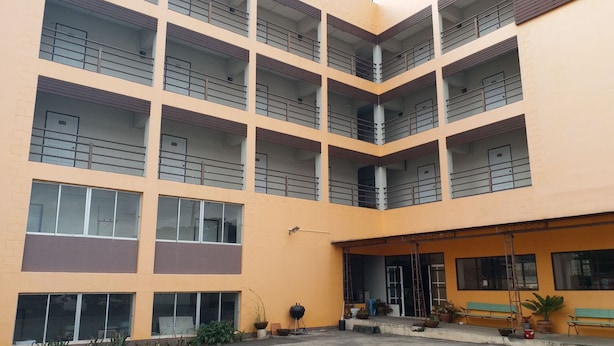 A multi-story building with balconies, large windows, and a covered entrance area with seating. - New Wanchai Hotel Pakchong (Pak Chong)