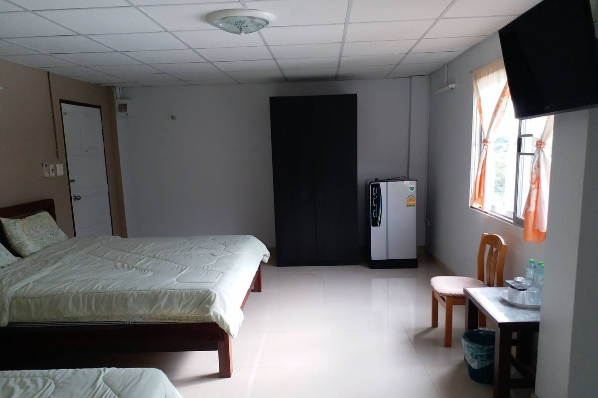 A hotel room with a bed, a desk with a chair, a refrigerator, and a television mounted on the wall.