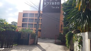 A building with a large sign, a gated entrance, and a concrete pathway leading to the building. - New Wanchai Hotel Pakchong (Pak Chong)