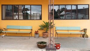 A building with two green benches and potted plants against a yellow wall. - New Wanchai Hotel Pakchong (Pak Chong)