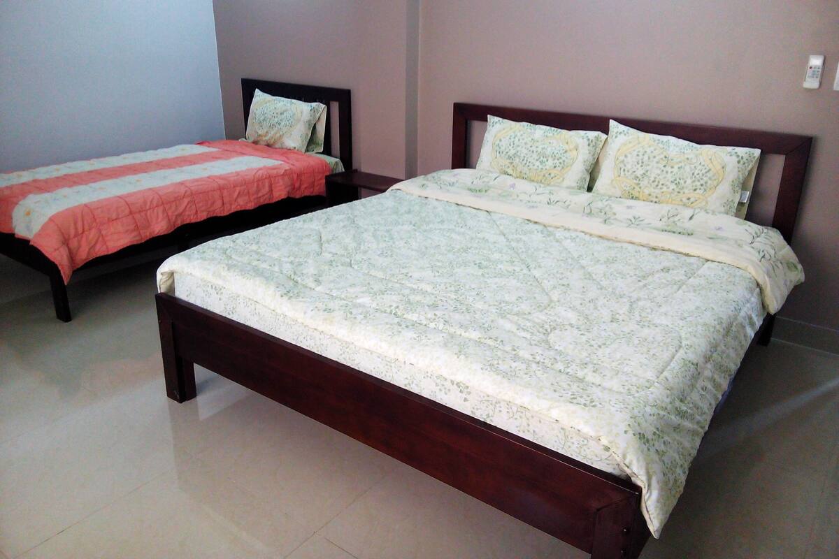 Two single beds with wooden frames and floral bedding, a tiled floor, and a plain wall with a light switch.