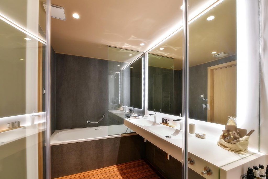 A modern bathroom with a glass shower enclosure, a white vanity with a large mirror, and a wooden floor.