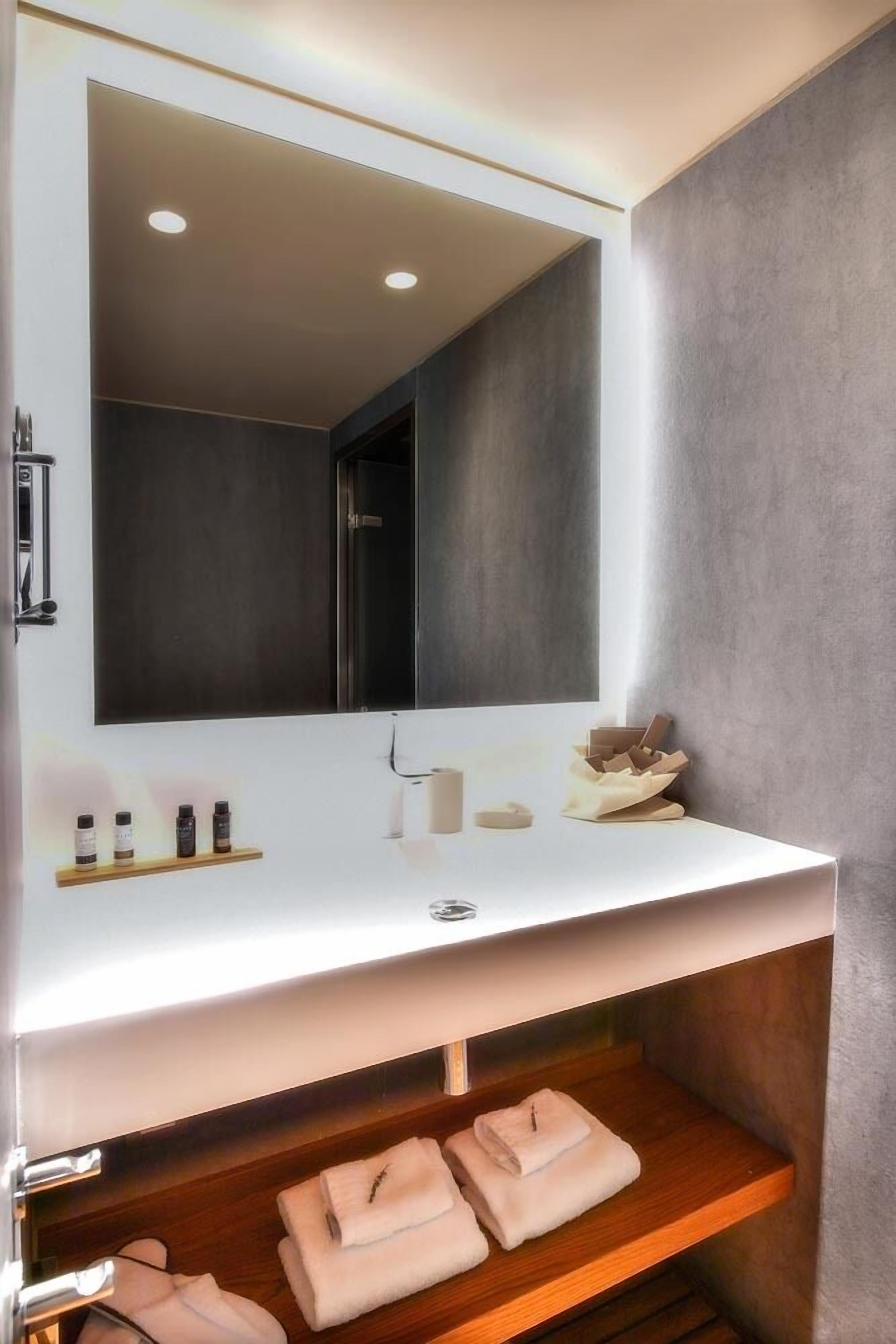 Un baño moderno con un espejo grande, lavamanos blanco y repisas de madera.