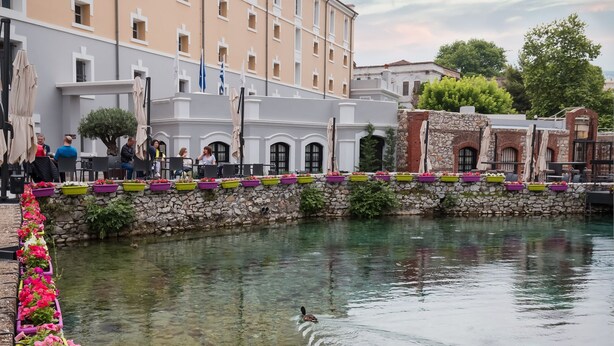 A canal with flower planters, a stone wall, and buildings in the background. - Hydrama Grand Hotel (Drama)