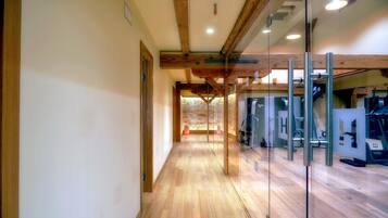 Un pasillo con suelo de madera y puertas de cristal que dan a un gimnasio con equipo de ejercicio.