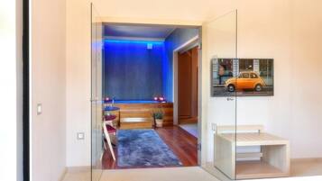A modern hotel room with a glass door leading to a bathroom, a small seating area with a pool table, and a framed picture on the wall.