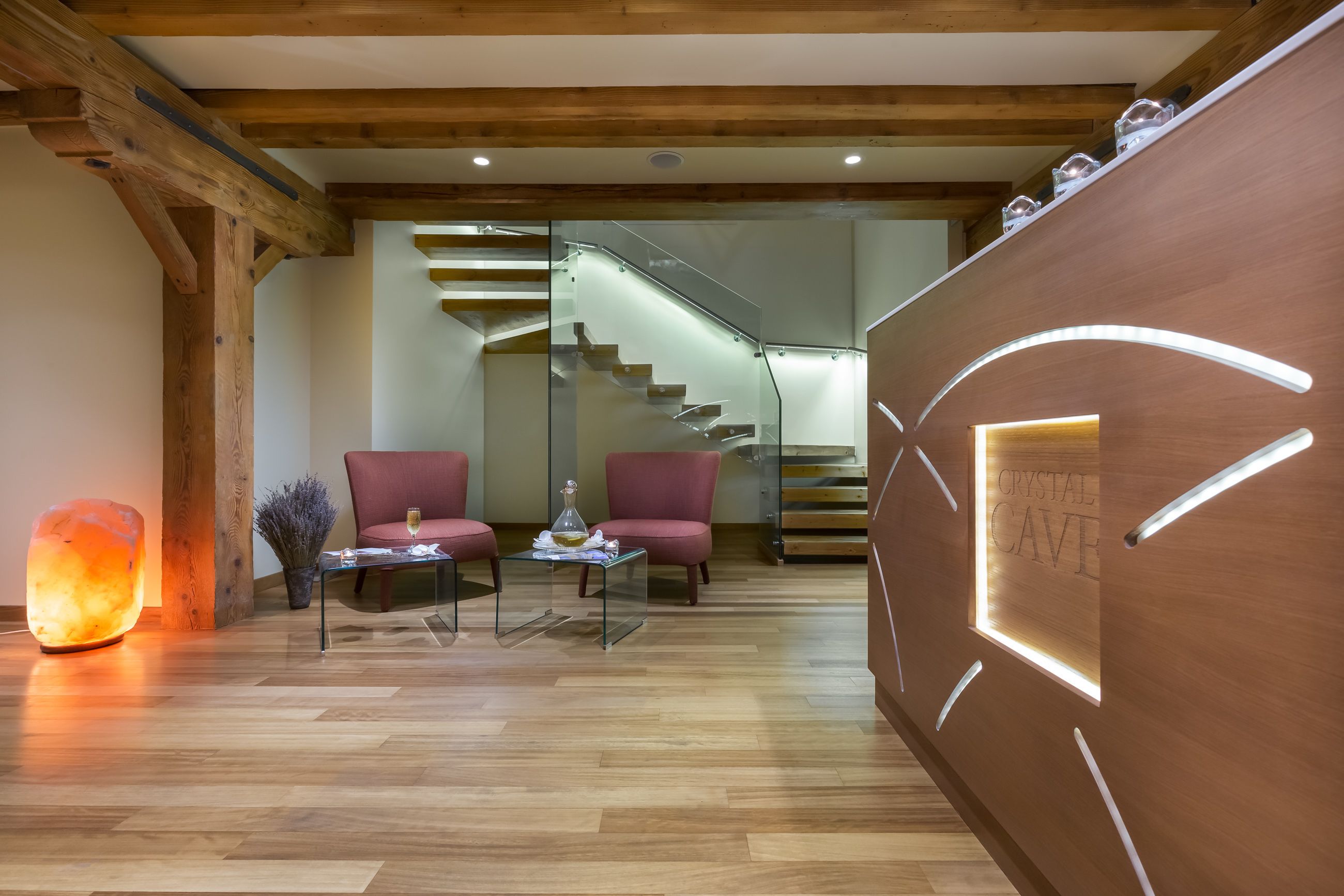 A modern interior with a wooden ceiling, a glass staircase, two red chairs, a glass table, and a heated floor.
