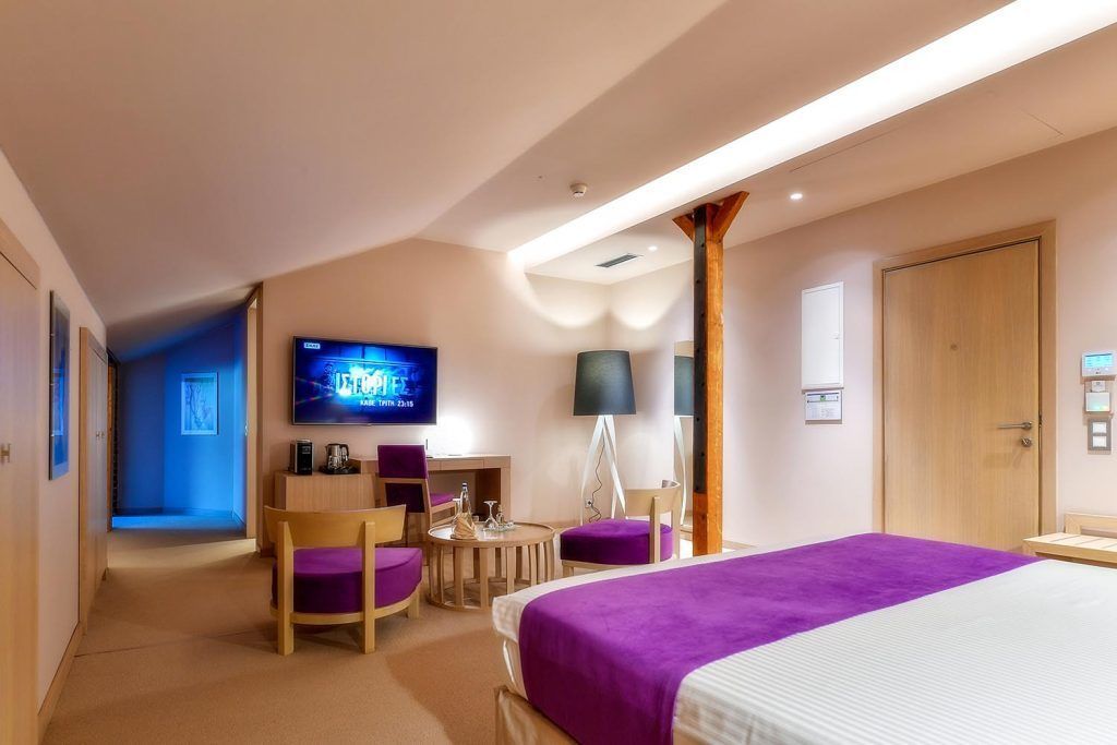 A hotel room with a bed, a desk with a chair, a television, and a lamp.