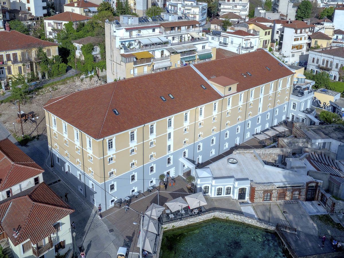 Un hotel de varios pisos con tejado de tejas rojas, situado en una zona urbana densamente construida con edificios circundantes.