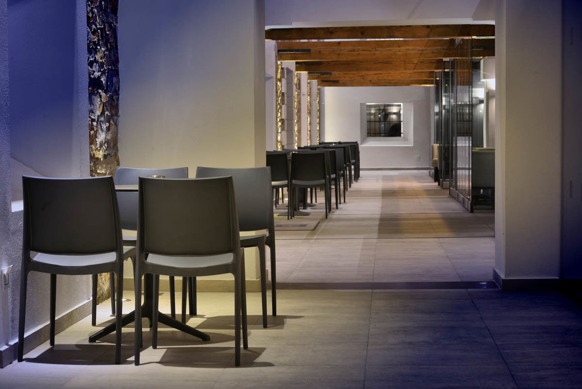 Un couloir d’hôtel moderne, avec une longue table et des chaises, des poutres en bois au plafond et un mur en verre d’un côté.