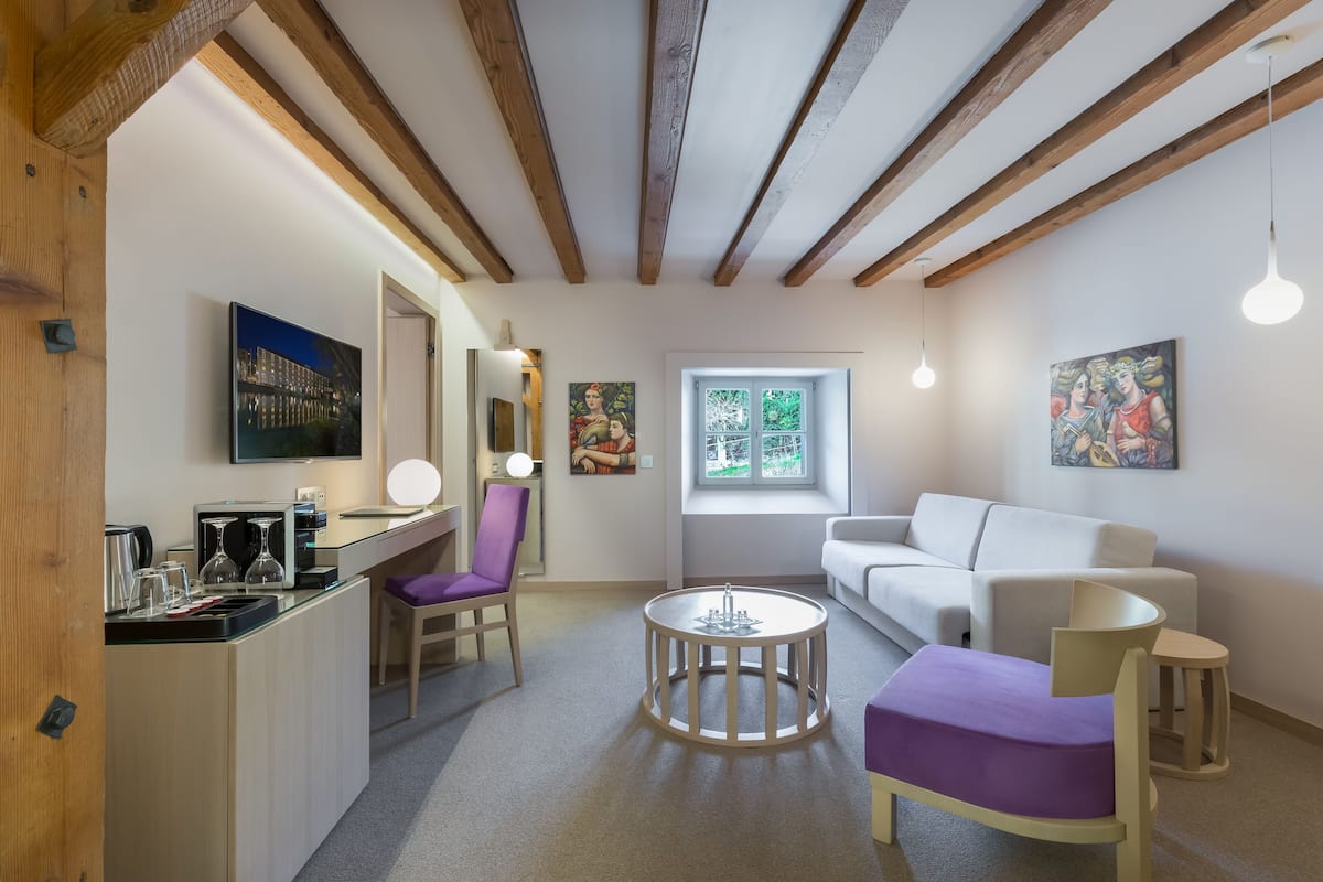 Ein modernes Zimmer mit Küchenzeile, einem runden Tisch, einer Couch und einem Fenster mit Blick auf Grünflächen.