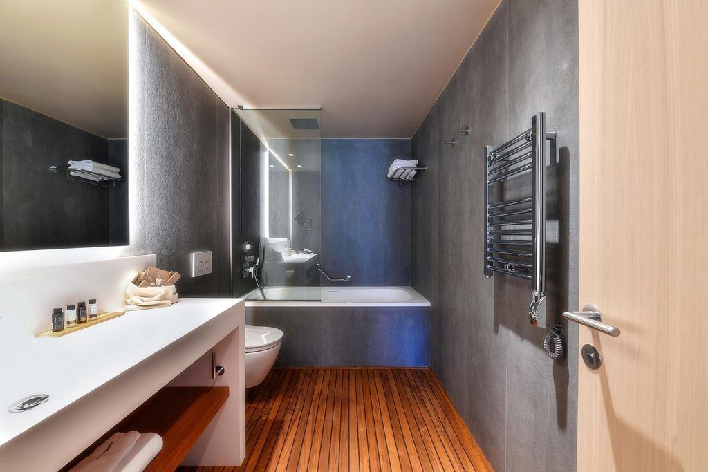 A modern bathroom with a wooden floor, a white sink with a mirror, a bathtub, and a towel rack.