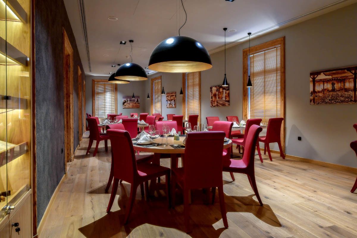 Un espace repas avec des chaises rouges et une table en bois, de grandes suspensions noires et des murs en bois ornés d’œuvres d’art.