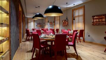 Un espace repas avec des chaises rouges et une table en bois, de grandes suspensions noires et des murs en bois ornés d’œuvres d’art.