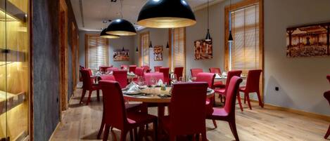 A dining area with red chairs and a wooden table, large black pendant lights, and wooden walls with artwork.