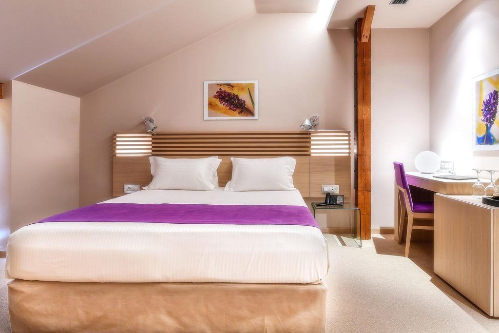 A modern hotel room with a large bed, a desk, and a chair.