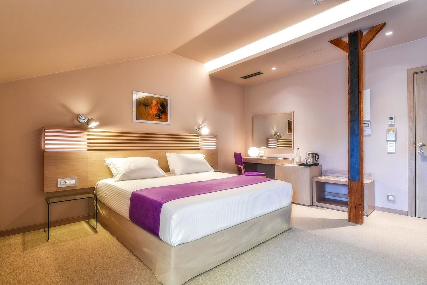 Quarto de hotel moderno com uma cama grande, mesas de cabeceira, toucador com espelho e escrivaninha com cadeira.