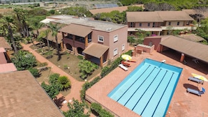 A swimming pool with a tiled deck, surrounded by buildings with red-tiled roofs and a view of a distant landscape. - Residence del Mare - Case Sicule (Ispica)