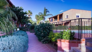A pathway leading to a building with a balcony, surrounded by well-maintained greenery and a tiled floor. - Residence del Mare - Case Sicule (Ispica)