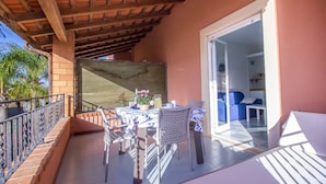 A balcony with a table and chairs, a blue sofa, and a glass door leading inside. - Residence del Mare - Case Sicule (Ispica)