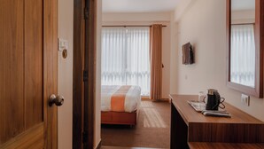 A hotel room with a wooden door, a bed with a white and orange bedspread, a desk with a coffee maker, and a TV on the wall. - Hotel Jagat (Kathmandu)