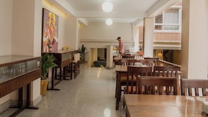 A spacious restaurant with wooden tables and chairs, a large painting on the wall, and a person standing near the counter. - Hotel Jagat (Kathmandu)