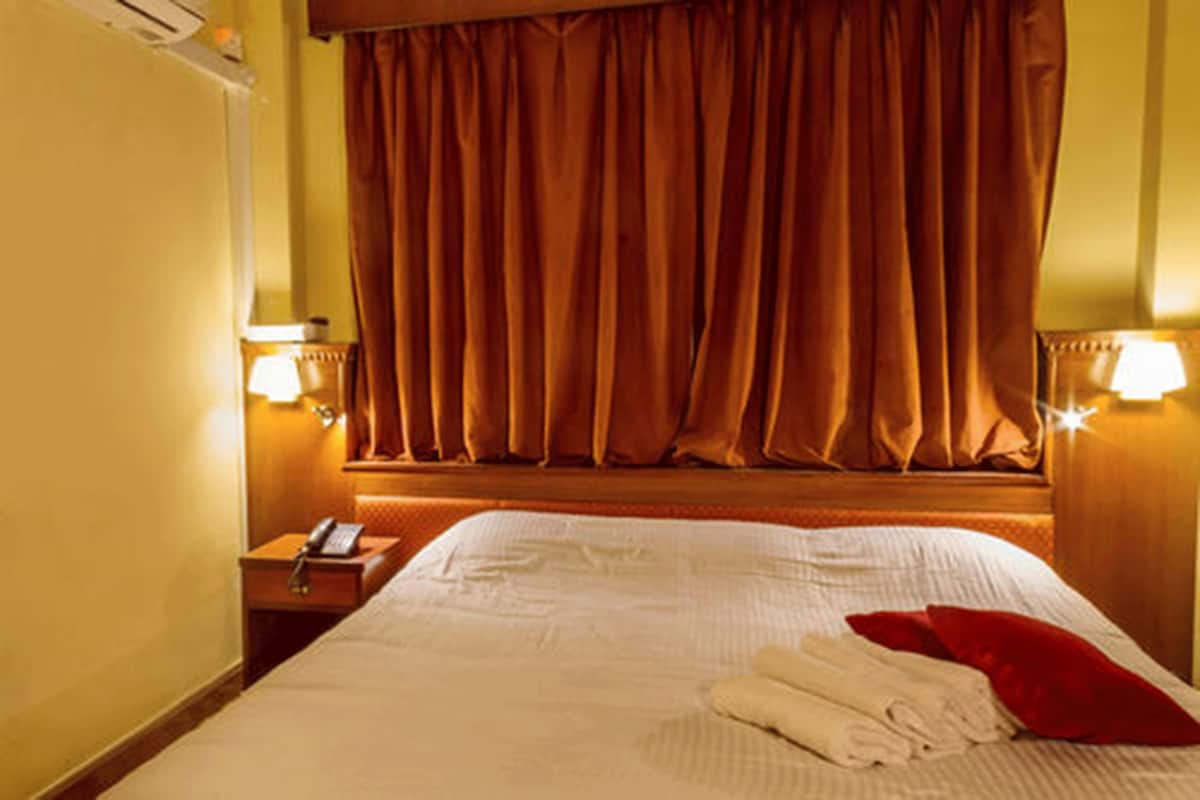 A hotel room with a large bed, a bedside table with a lamp, and a window with curtains.
