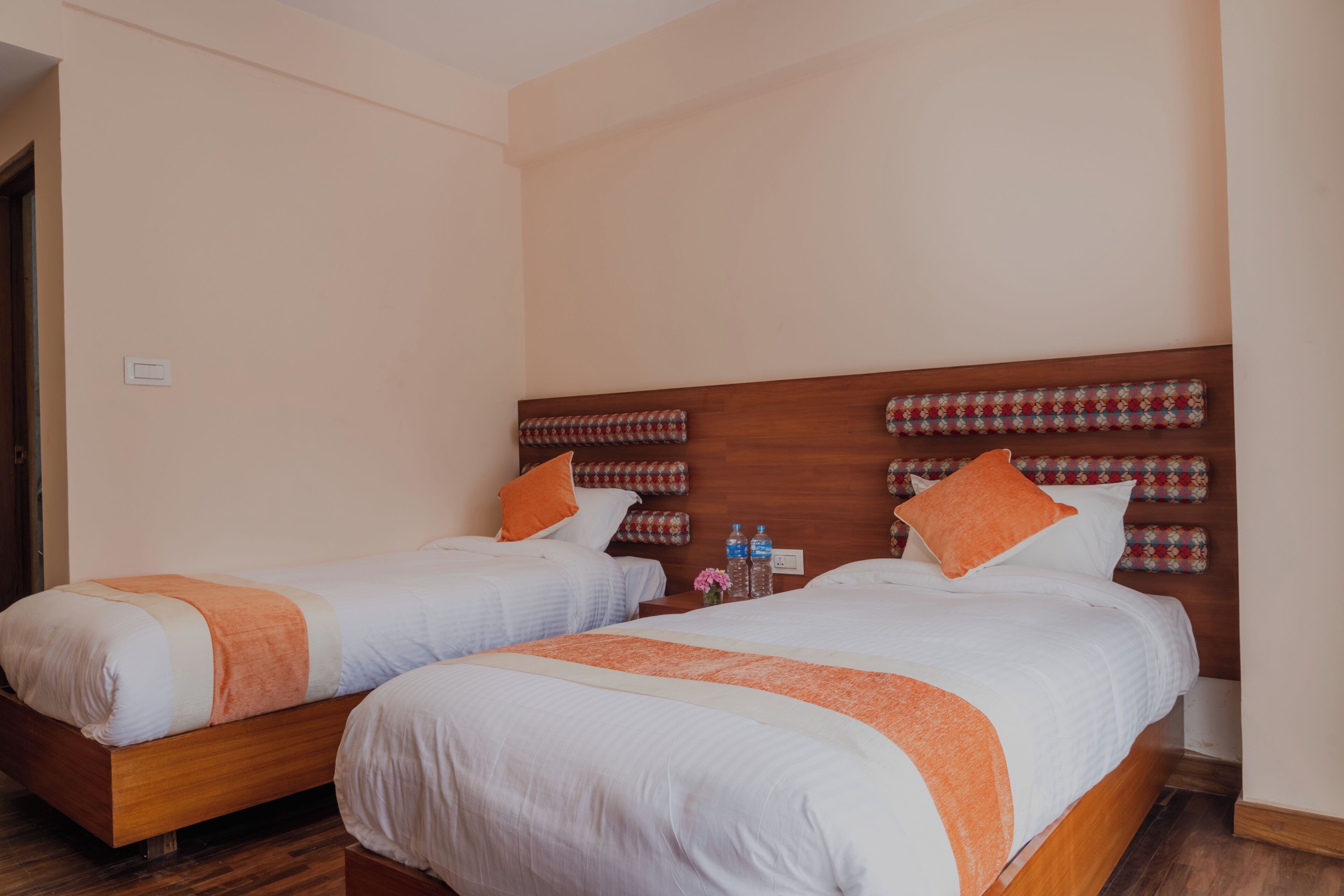 Duas camas de casal com cabeceiras de madeira, roupa de cama branca e detalhes em laranja.