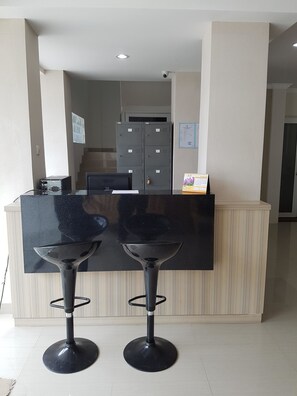A reception area with a counter, two bar stools, a computer, and a security camera. - Ethan Hotel (Jakarta)