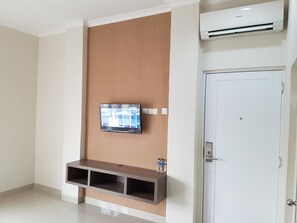 A room with a mounted TV, a wooden panel wall, a built-in shelf, and a door with a handle. - Ethan Hotel (Jakarta)