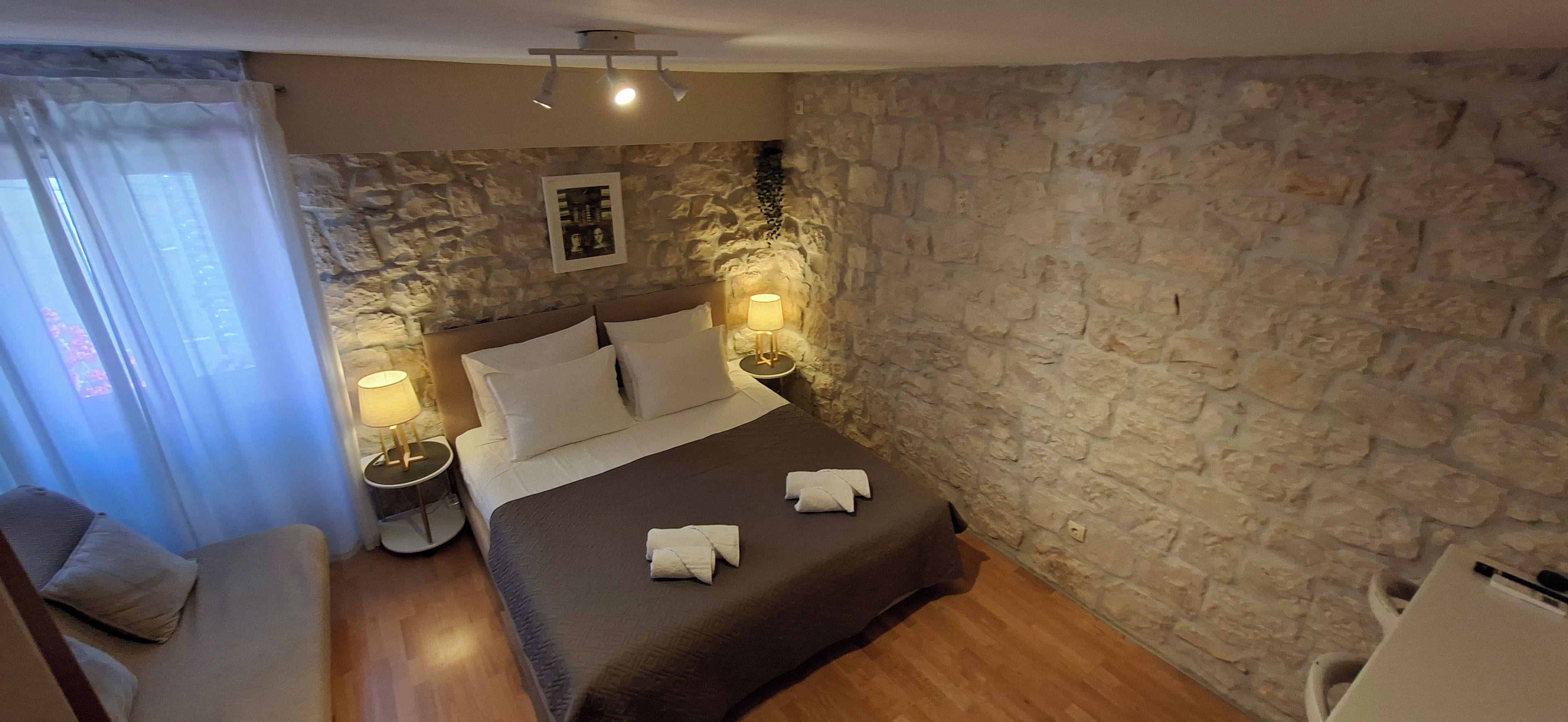 Ein Schlafzimmer mit Steinwand, einem Bett mit weißen Leinen, zwei Nachttischlampen und einem kleinen Tisch mit einer Lampe.