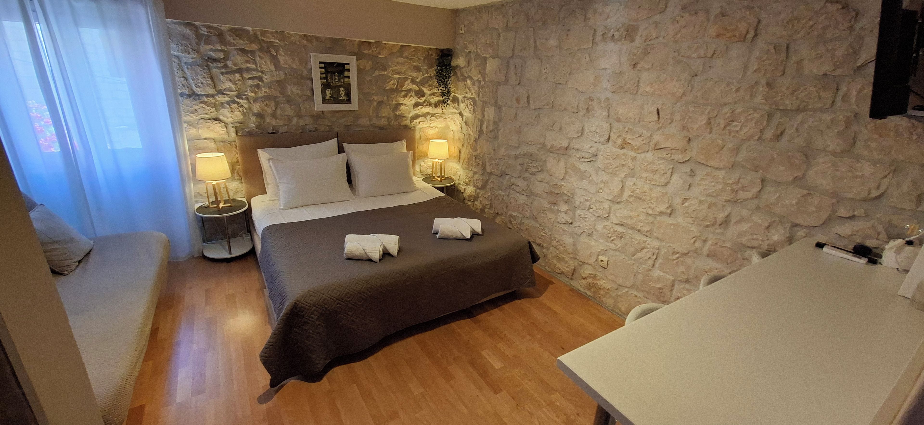 Une chambre d’hôtel avec un mur en pierre, un lit avec du linge de lit blanc, deux lampes de chevet et une petite table.