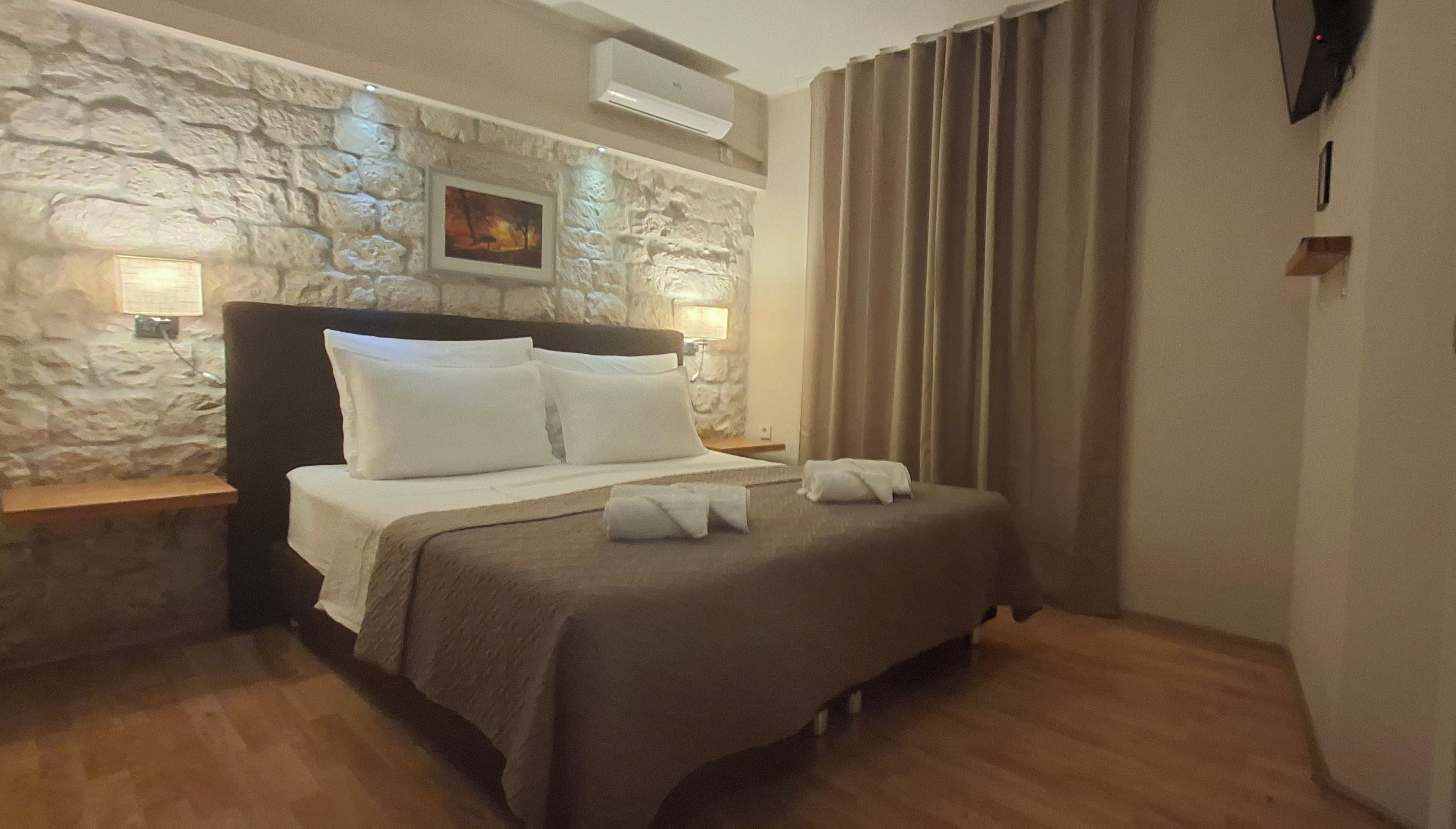 Habitación de hotel con pared de piedra, cama con ropa blanca, televisor de pantalla plana y piso de madera.